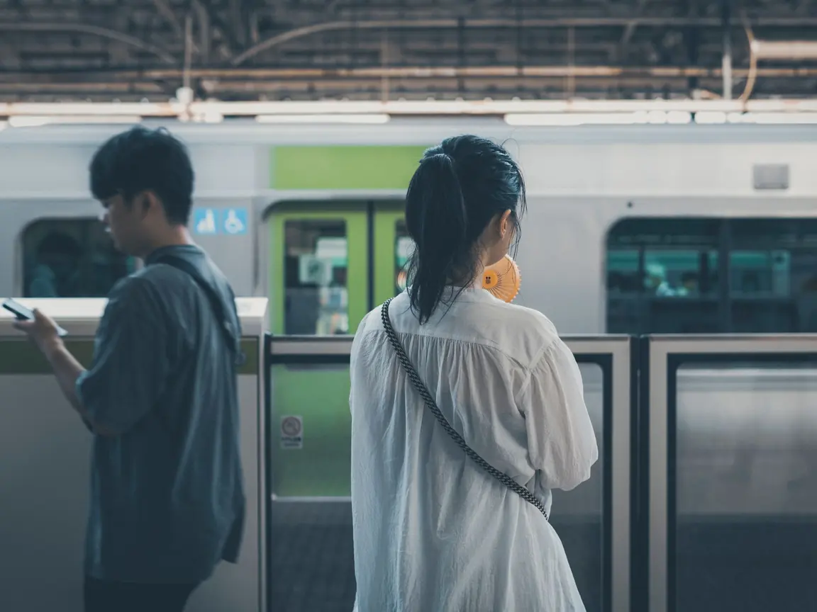 A young man checks his phone while a woman waits beside him on a Tokyo train platform
