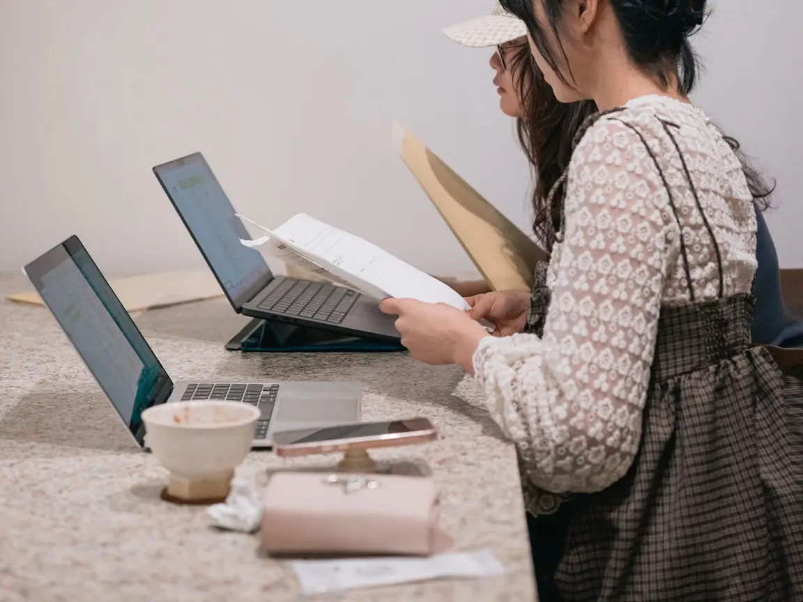Two students in Tokyo study at a shared table with laptops and printed notes